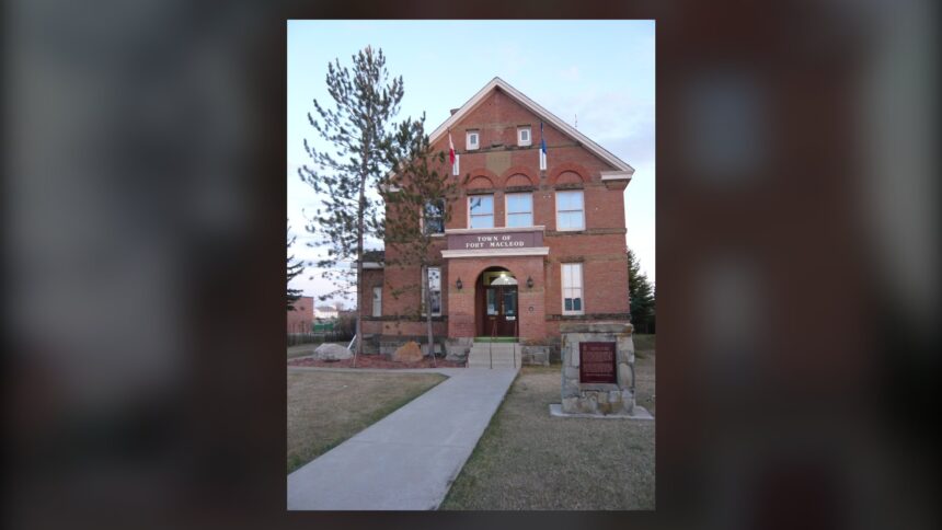 Red brick two-and-a-half-storey Territorial Court House in Fort Macleod with a central porch, a front walk and a stone marker, and a Town of Fort Macleod sign on the wall