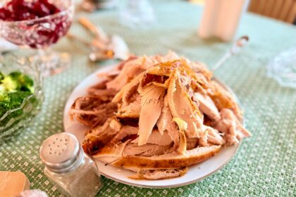 Platter of carved roast turkey on a Thanksgiving table with cranberry sauce and side dishes