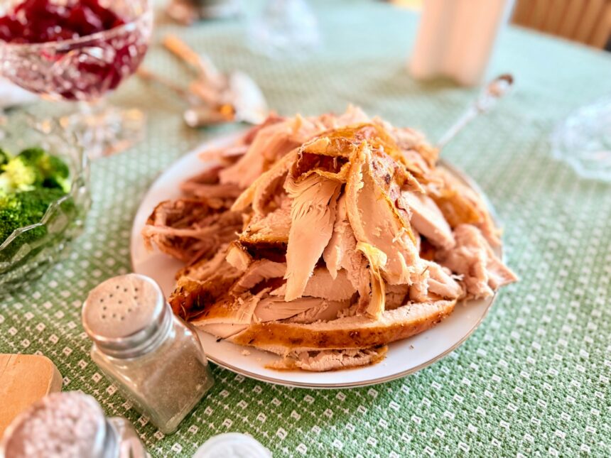 Platter of carved roast turkey on a Thanksgiving table with cranberry sauce and side dishes