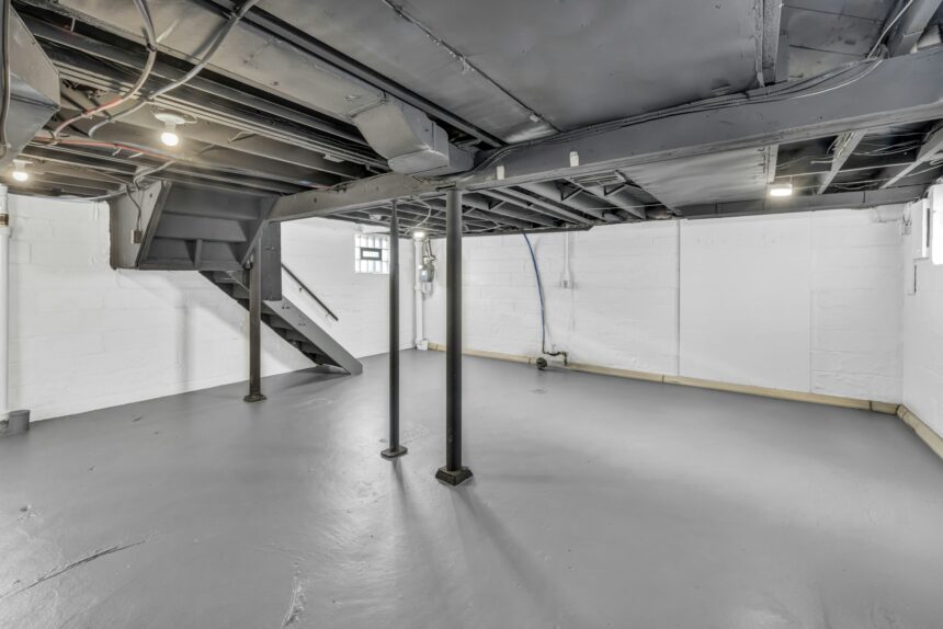 Unfinished basement with a painted concrete floor, steel support posts, exposed joists and a staircase