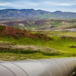 Large steel pipeline running across a green hillside landscape under a partly cloudy sky
