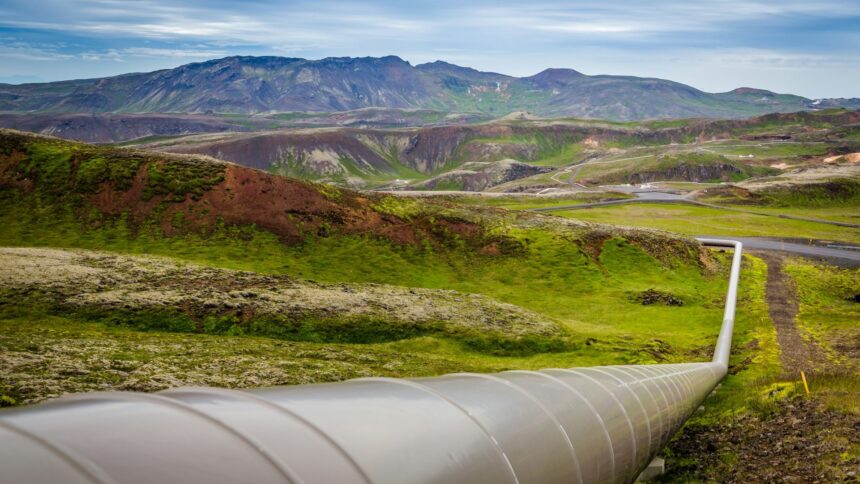 Large steel pipeline running across a green hillside landscape under a partly cloudy sky